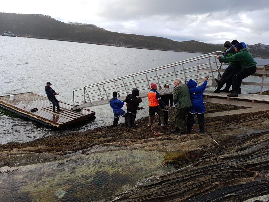 En gjeng arbeider med å ta inn landgangen til ei brygge ved sjøen