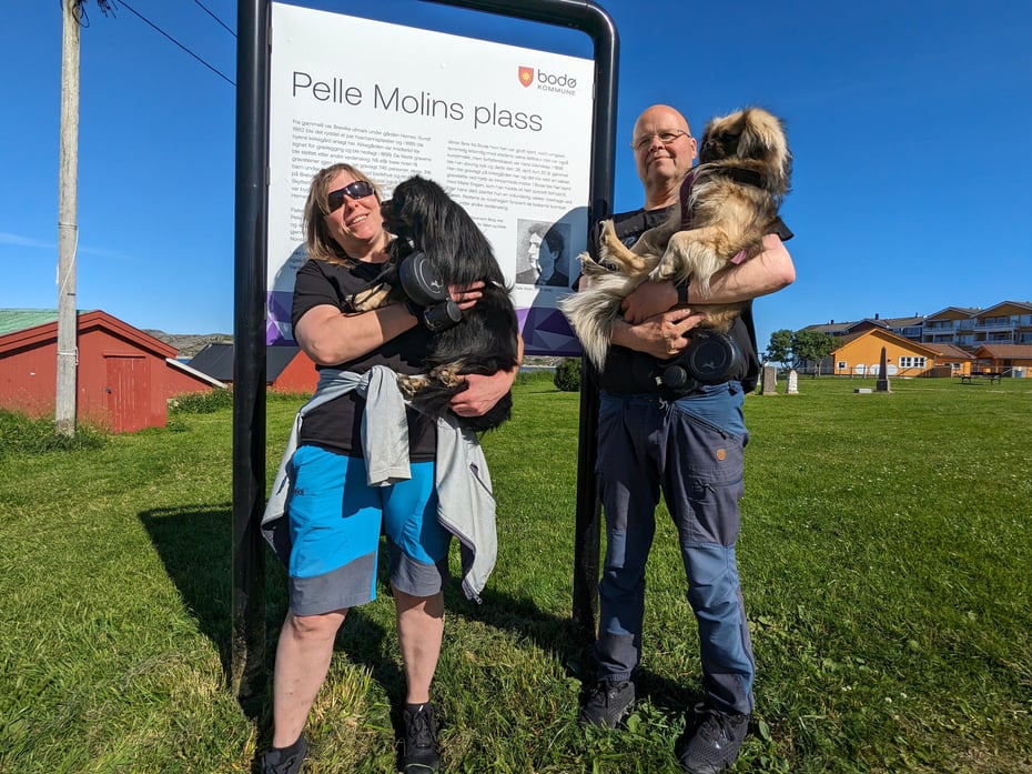 En mann og en dame som holder hver sin hund foran en informasjonsplakat