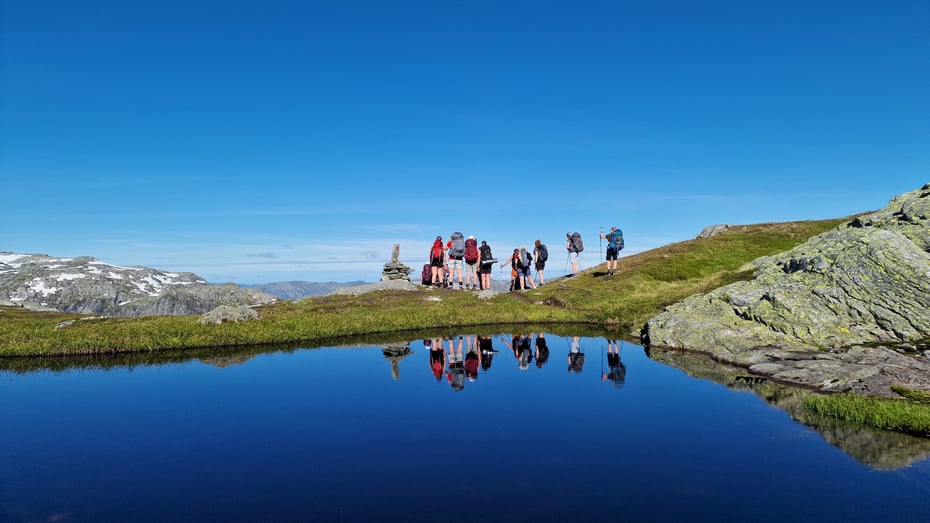 Gruppe mennesker går med vann og refleksjon foran.