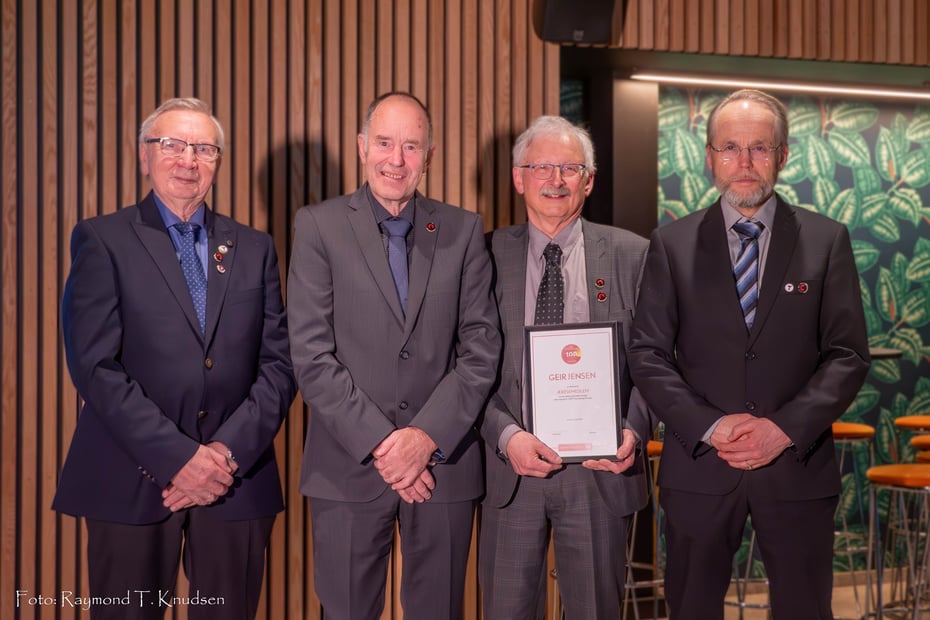 Fire voksne menn i dress hvor en av disse holder et diplom