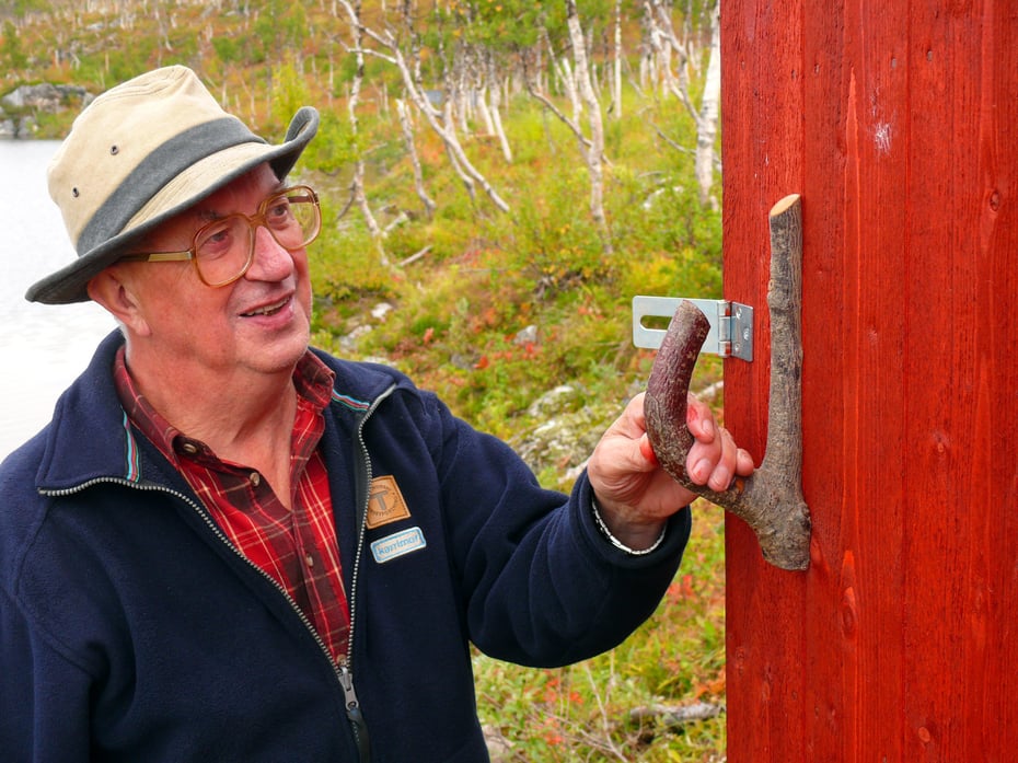 Eldre herre med hatt holder i naustdør med hjemmelaget dørhåndtak