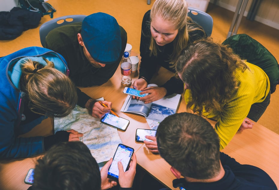 Personer sitter tett sammen rundt et bord og ser på kart og mobiltelefoner.