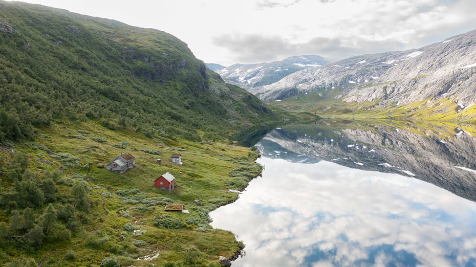 To små hytter ved et fjellvann som speiler fjellene.