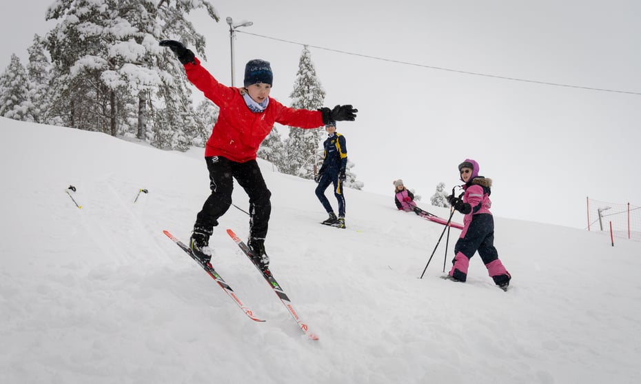 En jente med rød jakke hopper på ski.