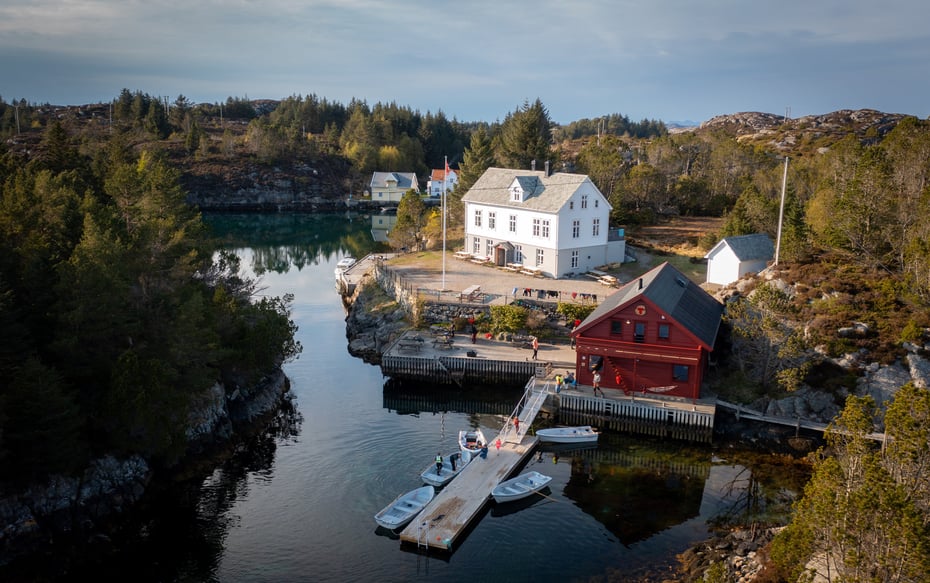 Stor, hvit hytte med naust og brygge på en øy.