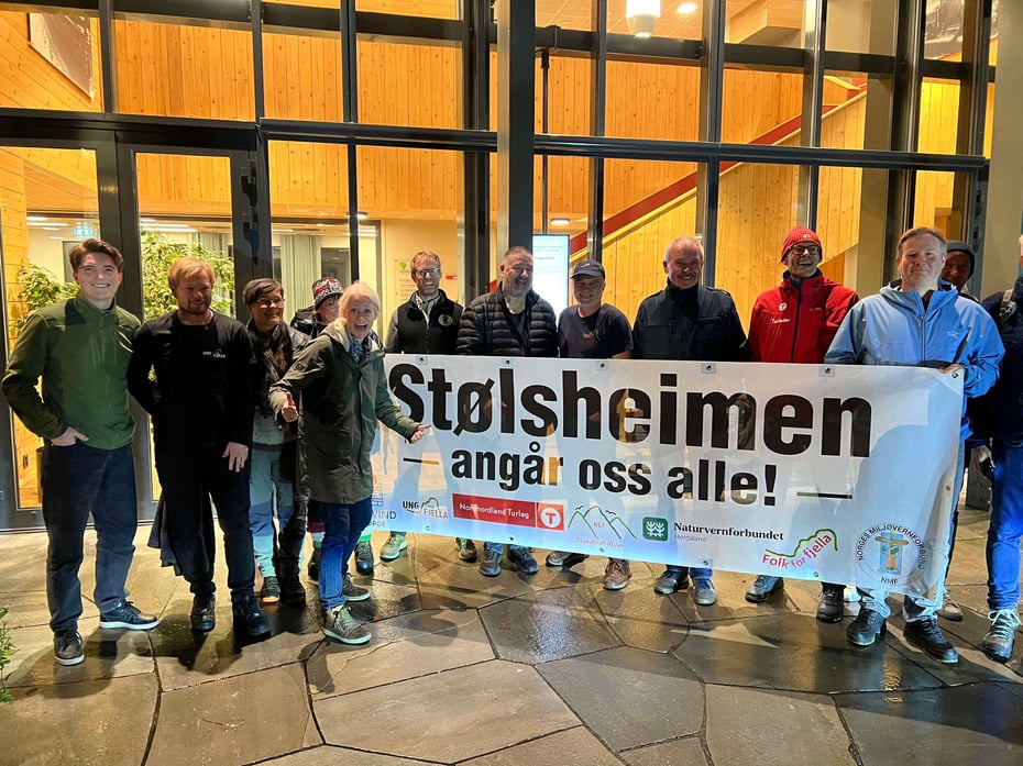 En gruppe personer med banner hvor det står Stølsheimen angår oss alle står utenfor et lokale om kvelden.