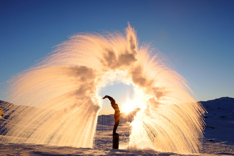 Person kaster snø i en bue rundt seg med solen bak.