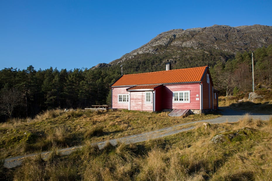 Rødmalt hytte foran fjell i lavlandet.