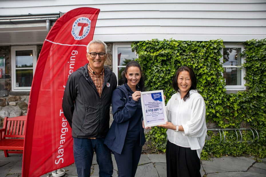 En mann og to damer står med en gavesjekk i hånden og smiler.