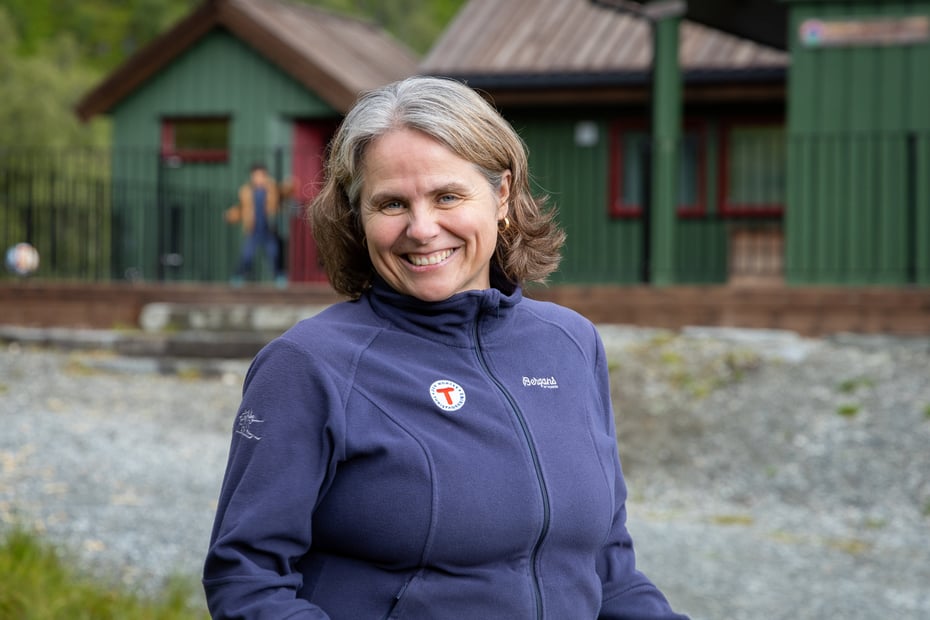 Dame med lilla genser smiler til kamera for en grønn hytte.