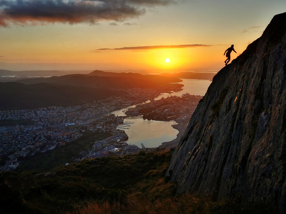Jogger på vei opp fjell i solnedgang.