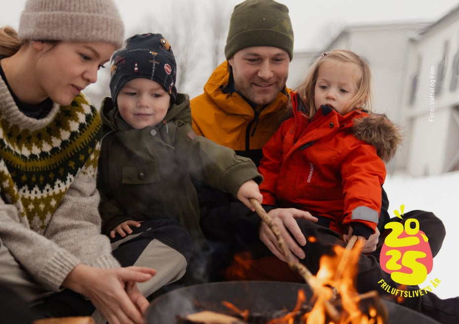 To voksne to barn koser seg rundt et bål midt på dagen.