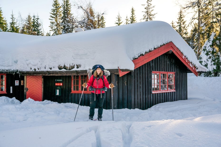 Skiløper foran en hytte med mye snø på taket