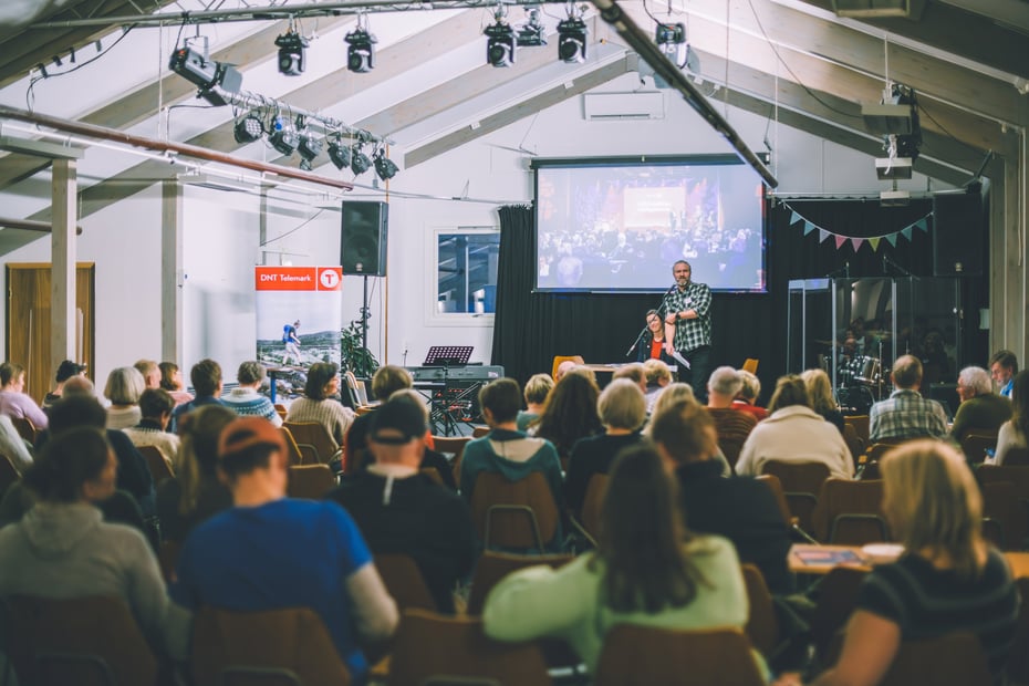 Mennesker sitter i en sal, det står en mann foran en skjerm. 