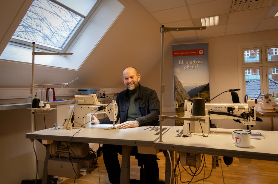 Mann ved symaskin smiler til kamera.