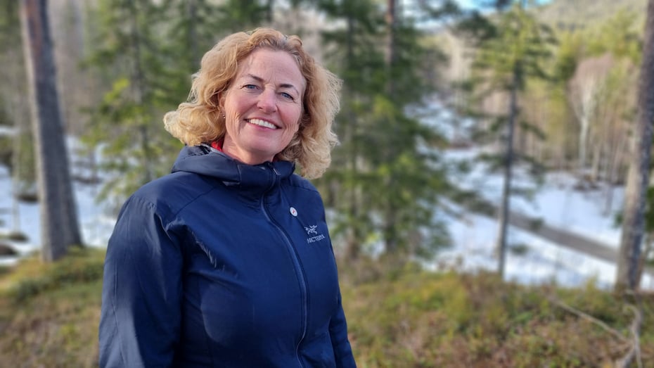 Dame som står ved skogen og smiler