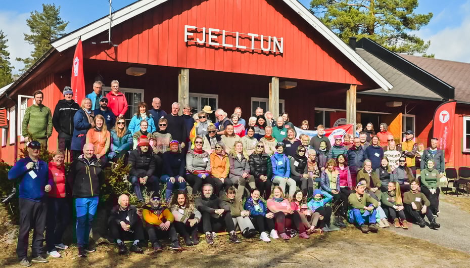 Gruppebilde av mange mennesker foran et rødt hus