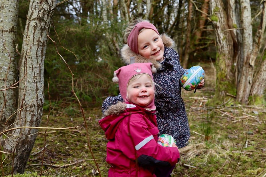 To barn på tur i skogen. De har vinterklær og påskeegg i hånden.