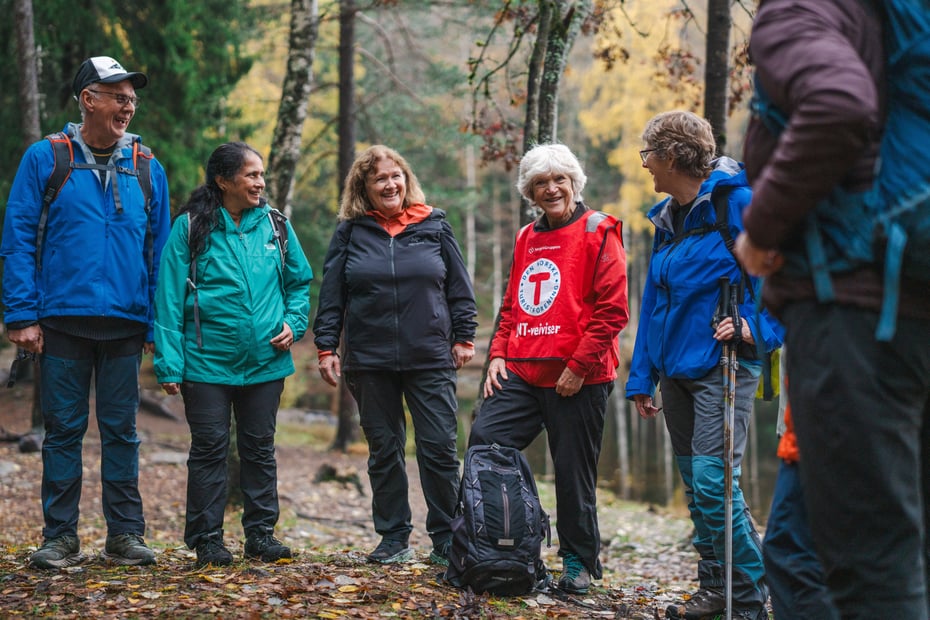 Fem mennesker står i skogen, de smiler. 