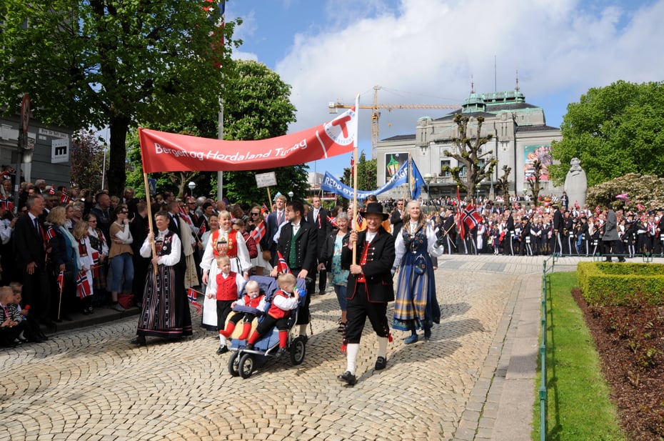 Turlagsmedlemme i 17. mai tog i Bergen med sol foran Den Nasjonale Scene.