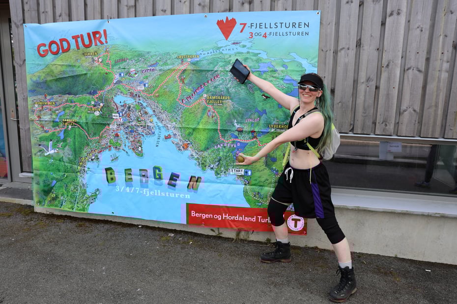 Dame med shorts, solbriller og caps viser frem ruten på 7-fjellsturen.