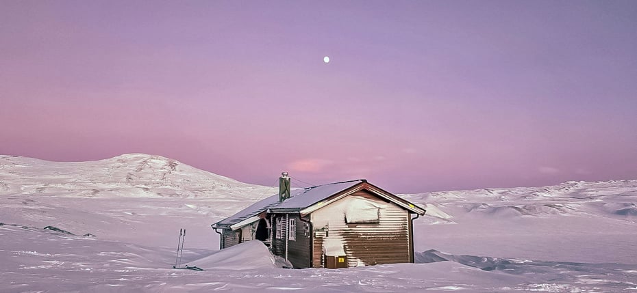 Bjellåvasstua dekket av snø og under rosa vinter himmel.