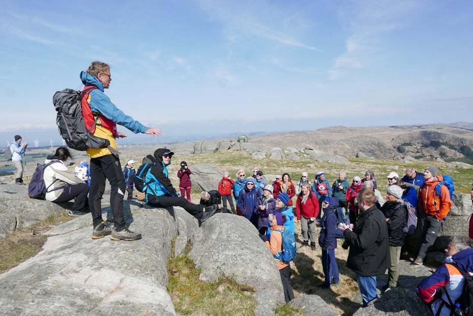 En mann står på en topp foran en stor folkemengde ute i storlått natur.
