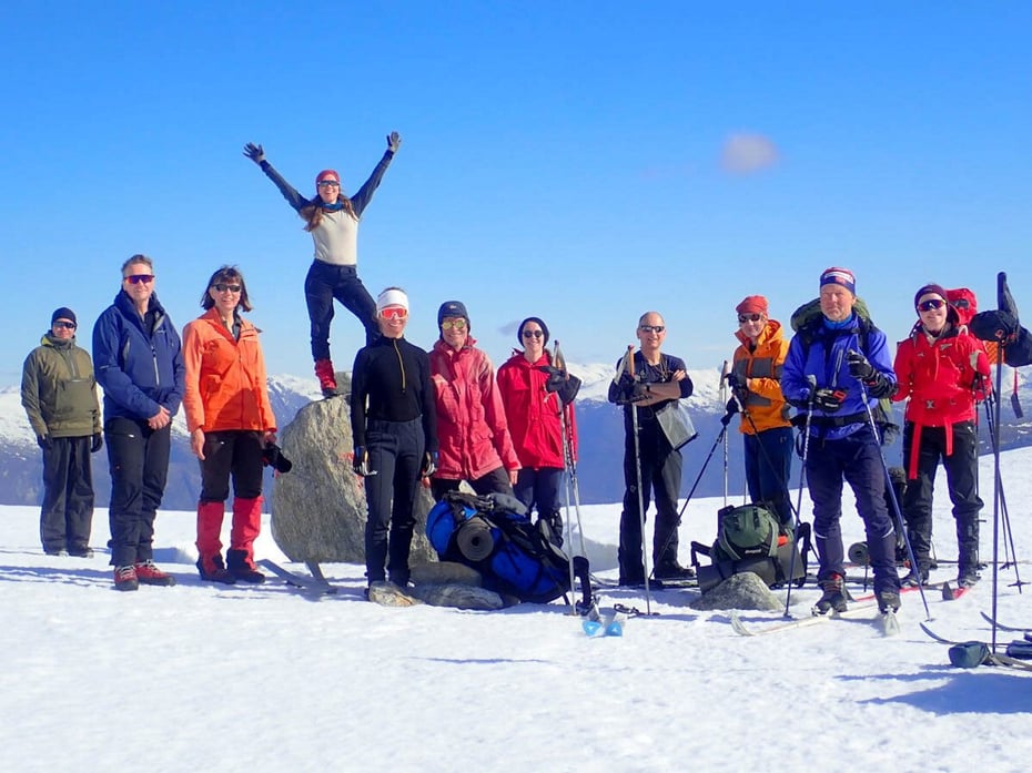En gruppe på snødekt fjelltopp i fint vær ser mot kamera.