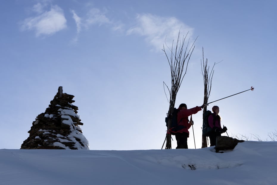 To personer på ski ved varde med kvist på ryggen, siluettbilde.