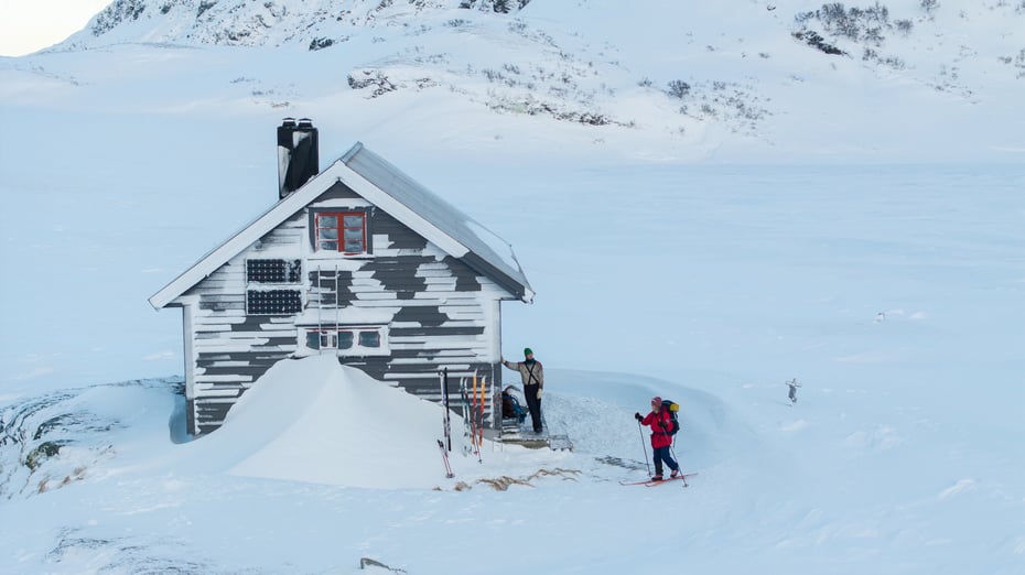 Hytte med snø og to personer utenfor.