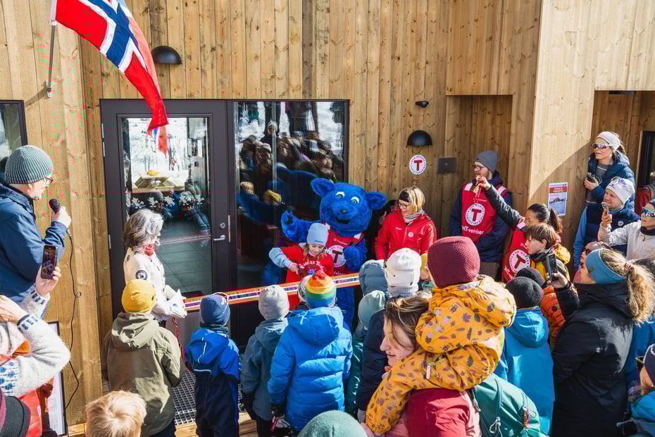 Ei jente klipper snoren foran døren på en ny og moderne hytte. Rundt henne står mange barn og voksne, og Barnas turlag sin maskot, den blå fjellreven Turbo.
