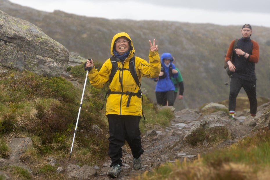 Asiatisk dame i gul goretex-jakke på fjelltur i regn.