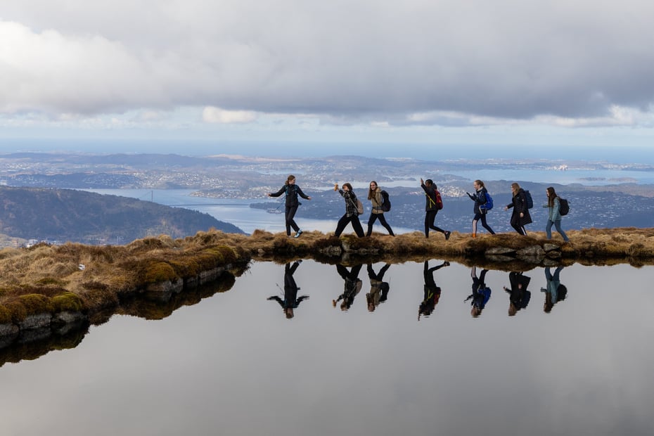 Ungdommer på rekke ved fjellvann.