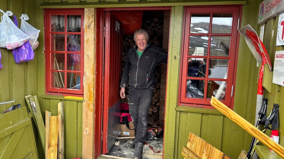 Mann  smiler i skitne arbeidsklær på hytte.