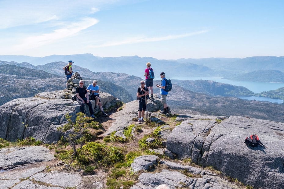 Mennesker står sammen på et fjell med utsikt til fjell og fjord