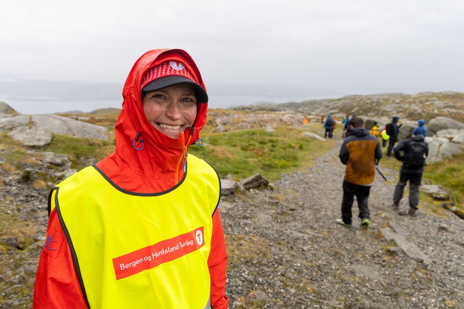 Kvinne i gul vest smiler til kamera under 7-fjellsturen.