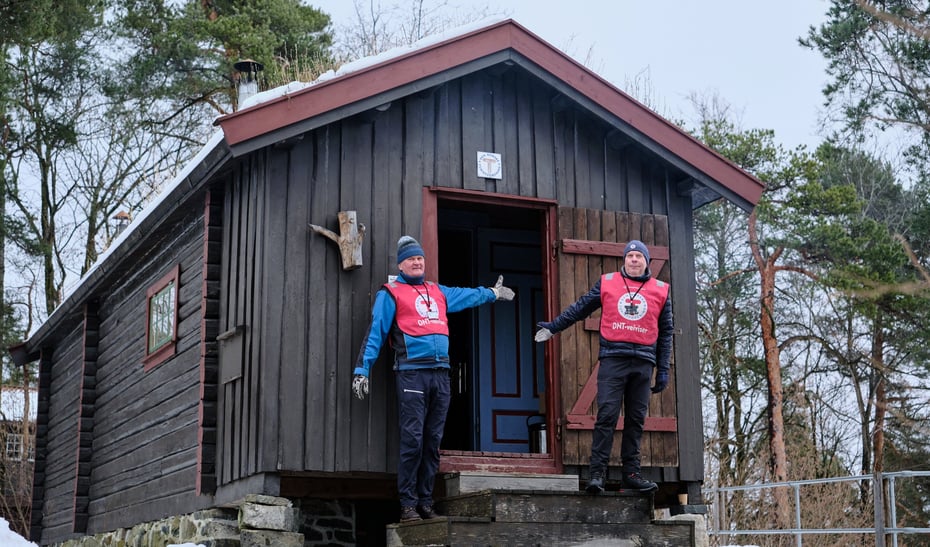 To hyttevakter ønsker velkommen inn i brun hytte.