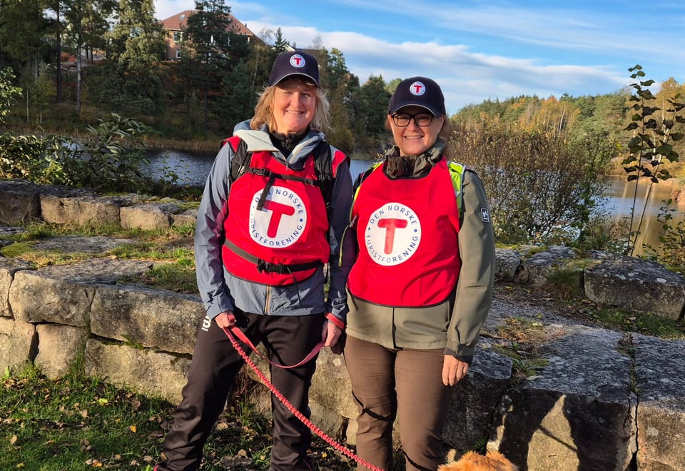 To kvinner i rød turledervest fra DNT på tur med hund. Foto.