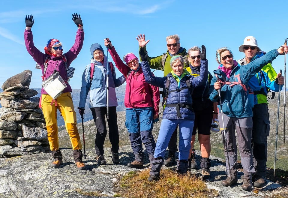 Gjeng glade turgåere med hendene i været på toppen av et fjell.
