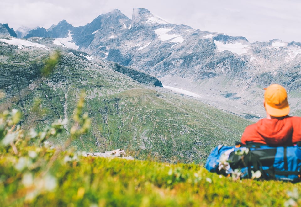 Mann med caps og rød jakke som ser utover fjellet. 