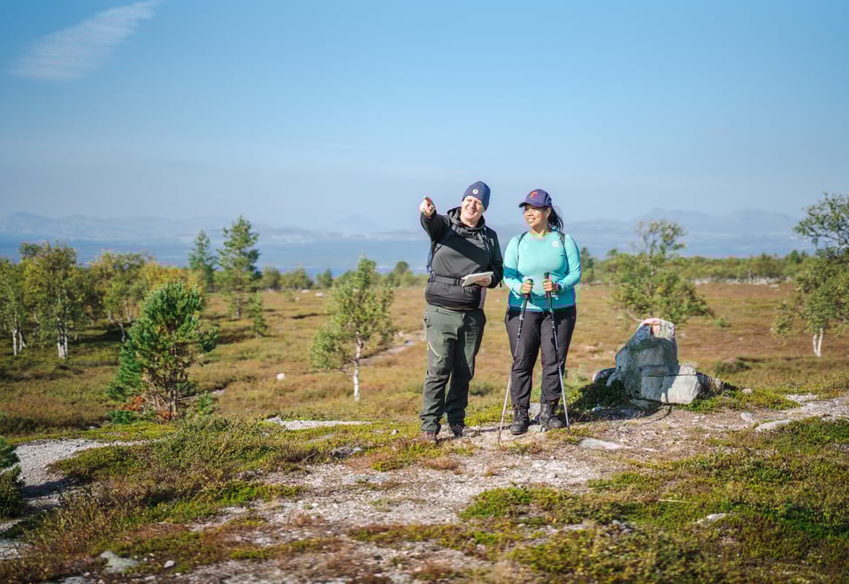 To personer som ser dit mannen peker. De står i et fjellområde, det er blå himmel