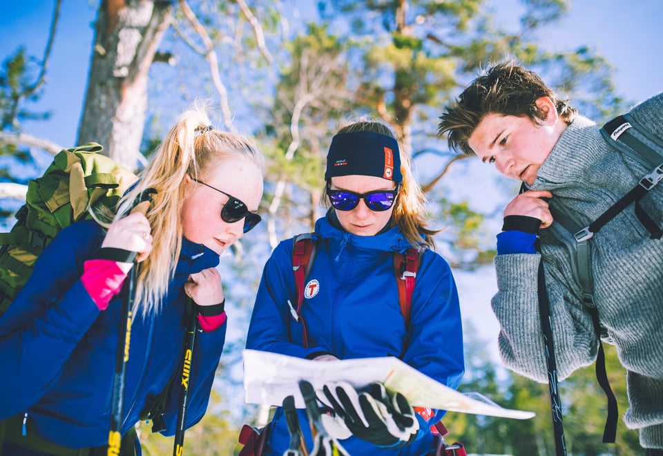 Tre ungdommer studerer kart ute i naturen