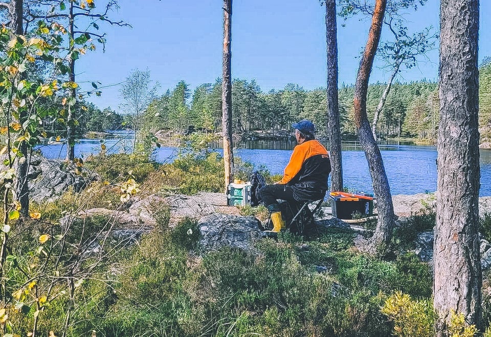 En mann sitter på en stolsekk i skogen og speider utover vannet.