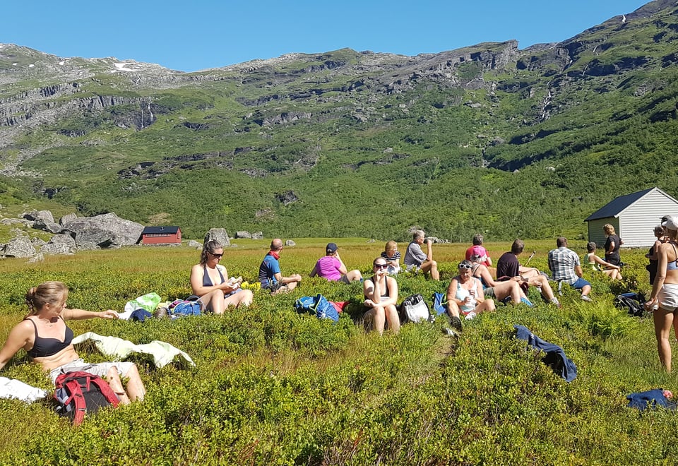 Folk som slappa av i lyngen, med fjell i bakgrunnen og blå himmel