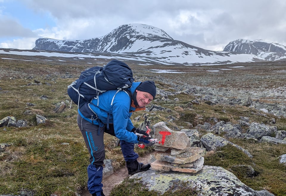 Mann maler rød T på stein langs sti i fjellet 
