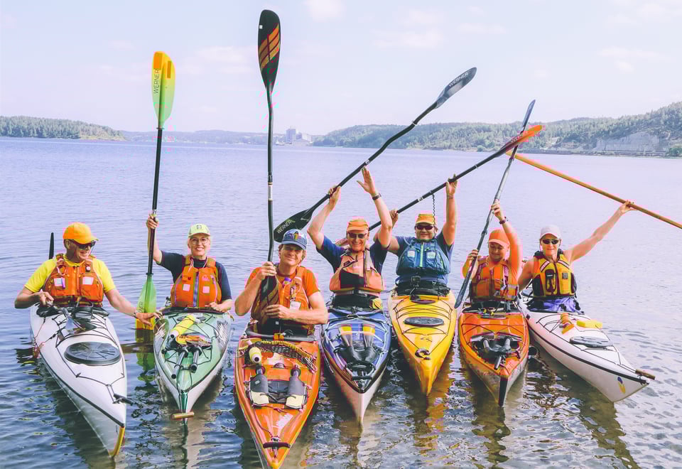 Sju kajakkpadlere side om side med padleåre løftet opp i luften.