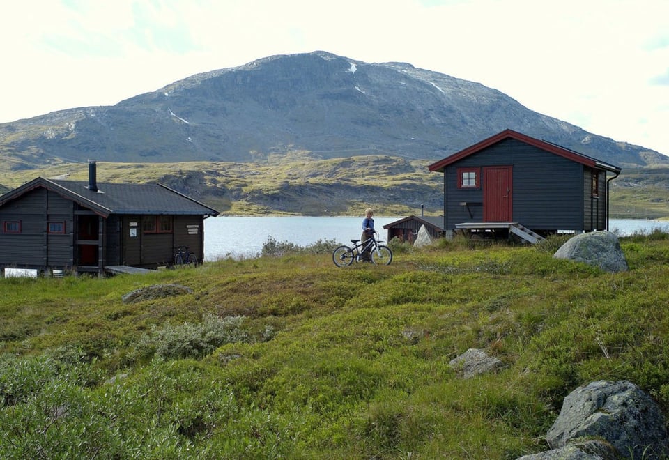 To hytter ved vann med fjell i bakgrunnen