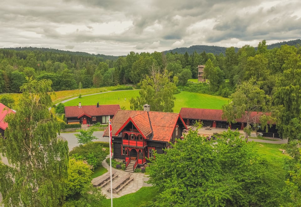 Dronebilde over området. Sommer. Hovedhus i front.