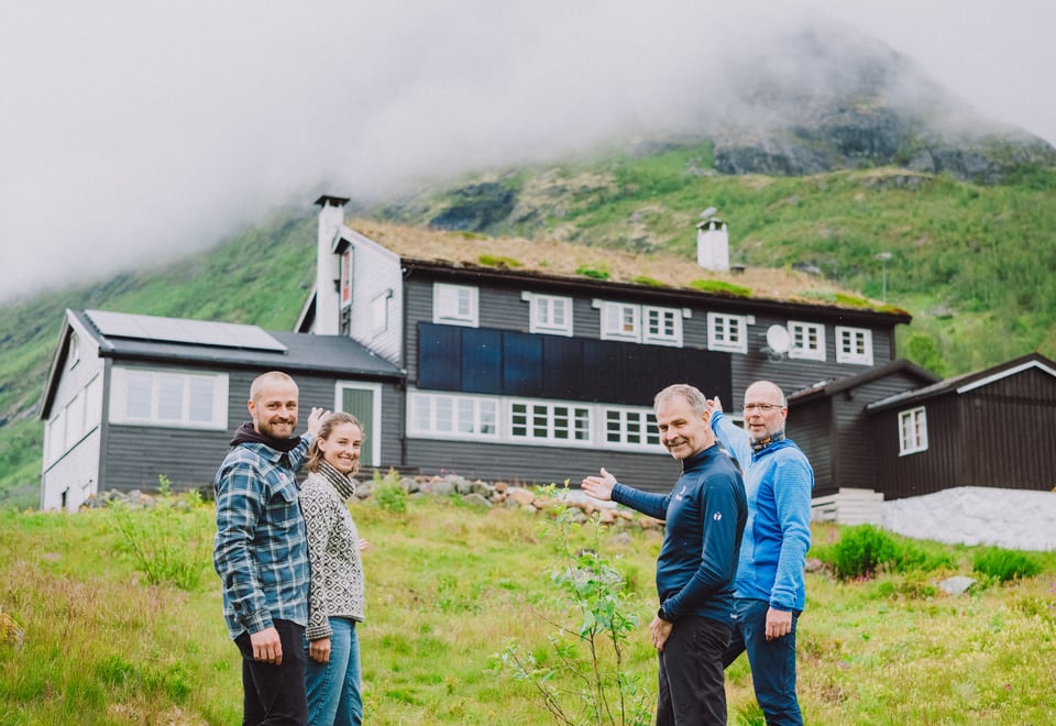 Fire personer foran DNT hytta Skogadalsbøen. Peker stolt på nye solceller på tak og vegger.