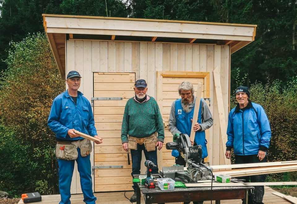 Fire menn i arbeidstøy utenfor en nybygd utedo. Foto.